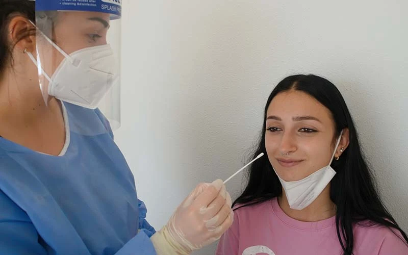 Picture of two people taking a nasal swab as part of the Corona test. On the right is a woman having the test done. On the left is a lady in protective clothing taking the smear.